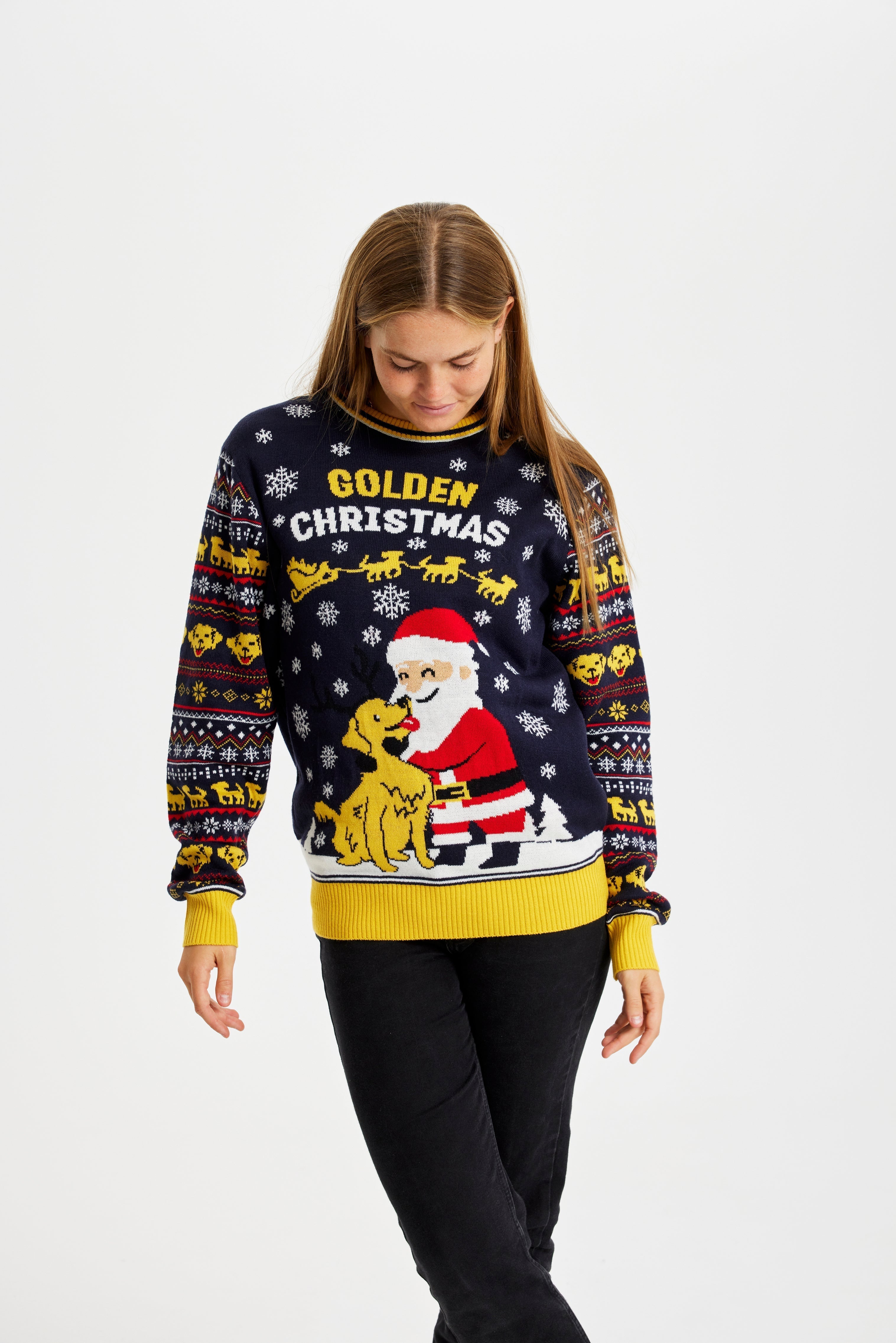 Una donna in posa che indossa un maglione natalizio giallo e blu con un Babbo Natale e un cane.
